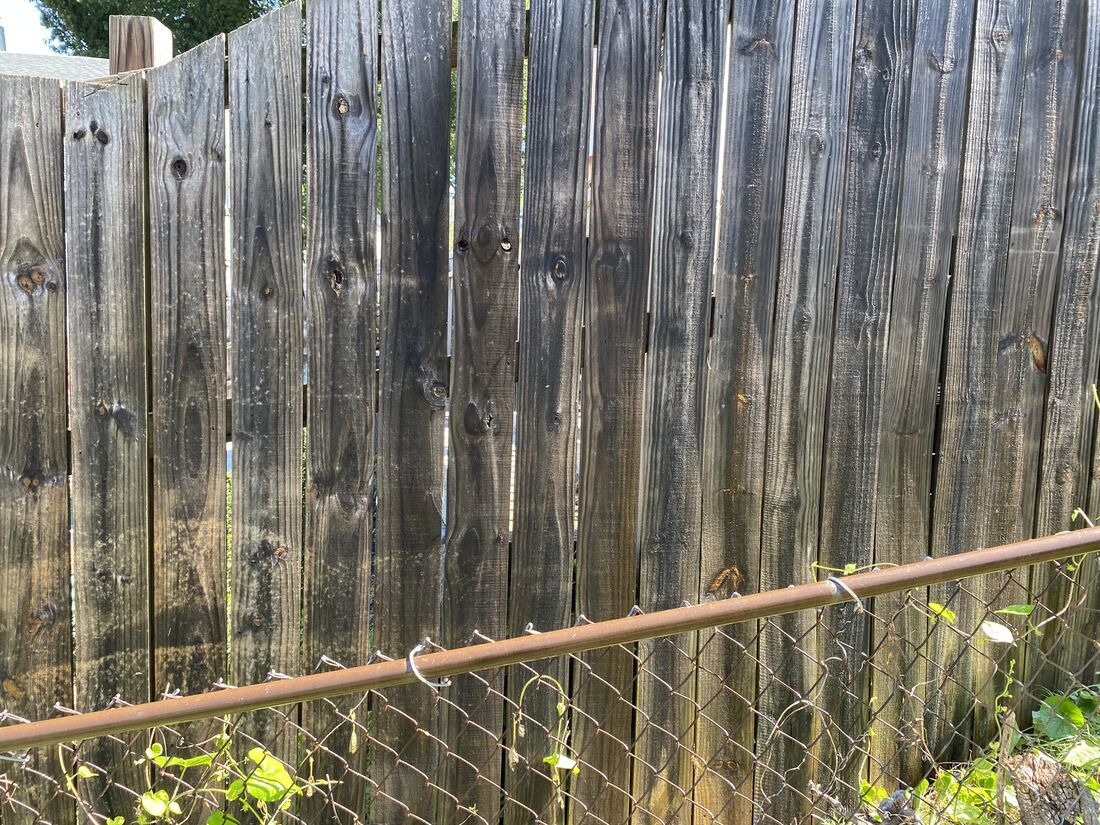 Severely weathered black fence boards showing UV damage and moisture deterioration